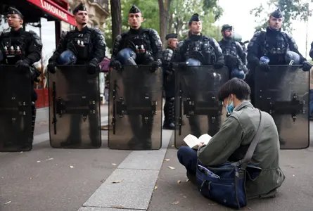 A demonstrator sits reading a book in front of gendarmerie officers holding riot shields