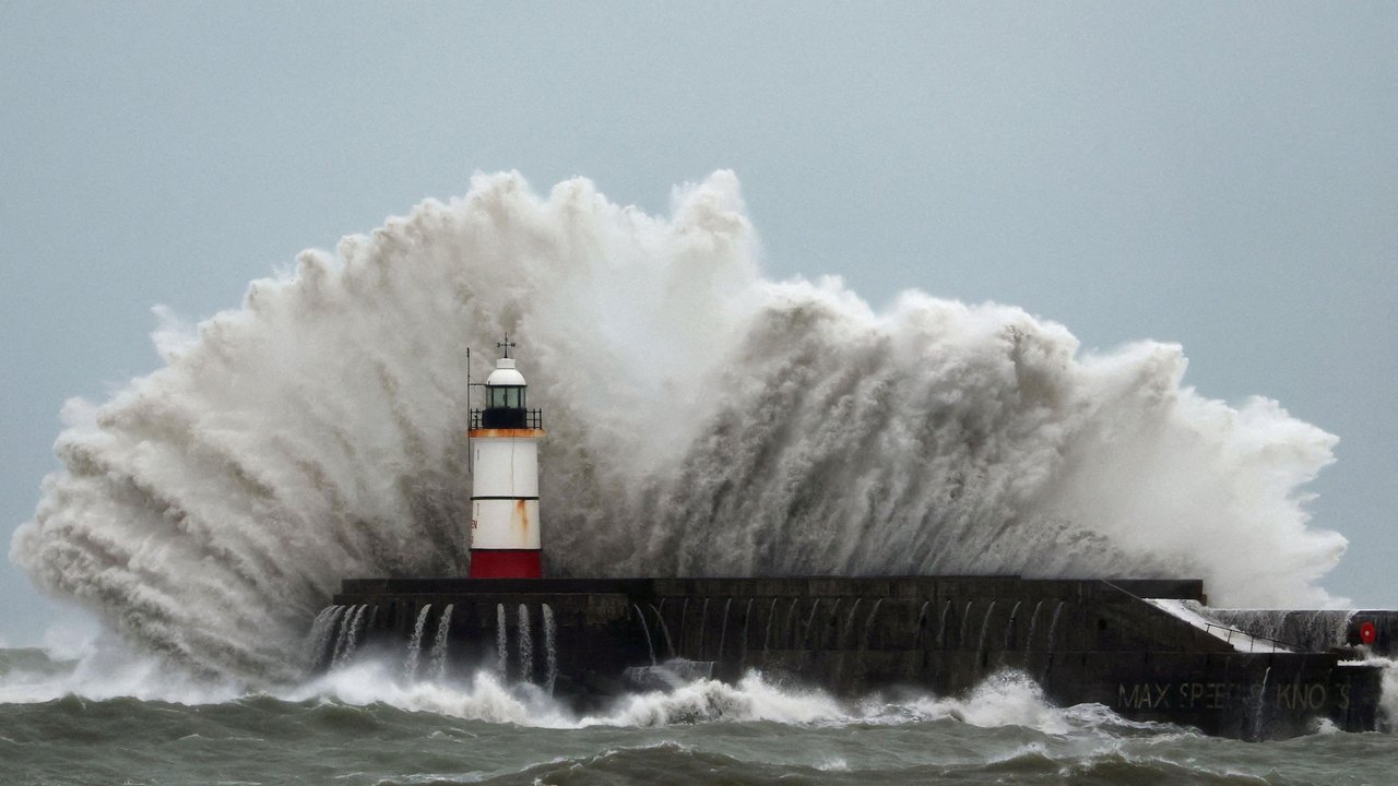 A wave crashes dramatically over a lighthouse