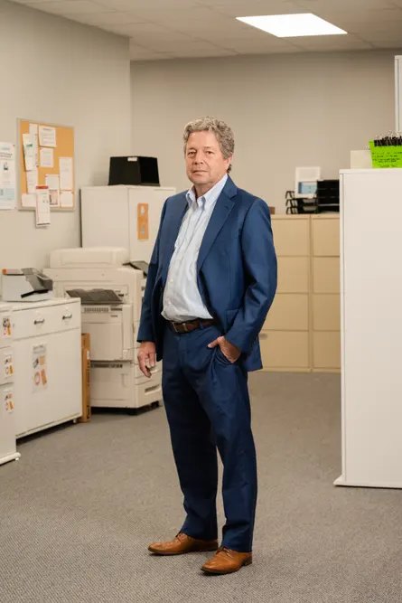 man in blue suit stands in office with one hand in pocket