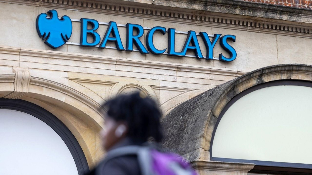 The Barclays logo is seen on the outside of a branch in London as a passer-by walks down the street in the foreground, taken in 2024.