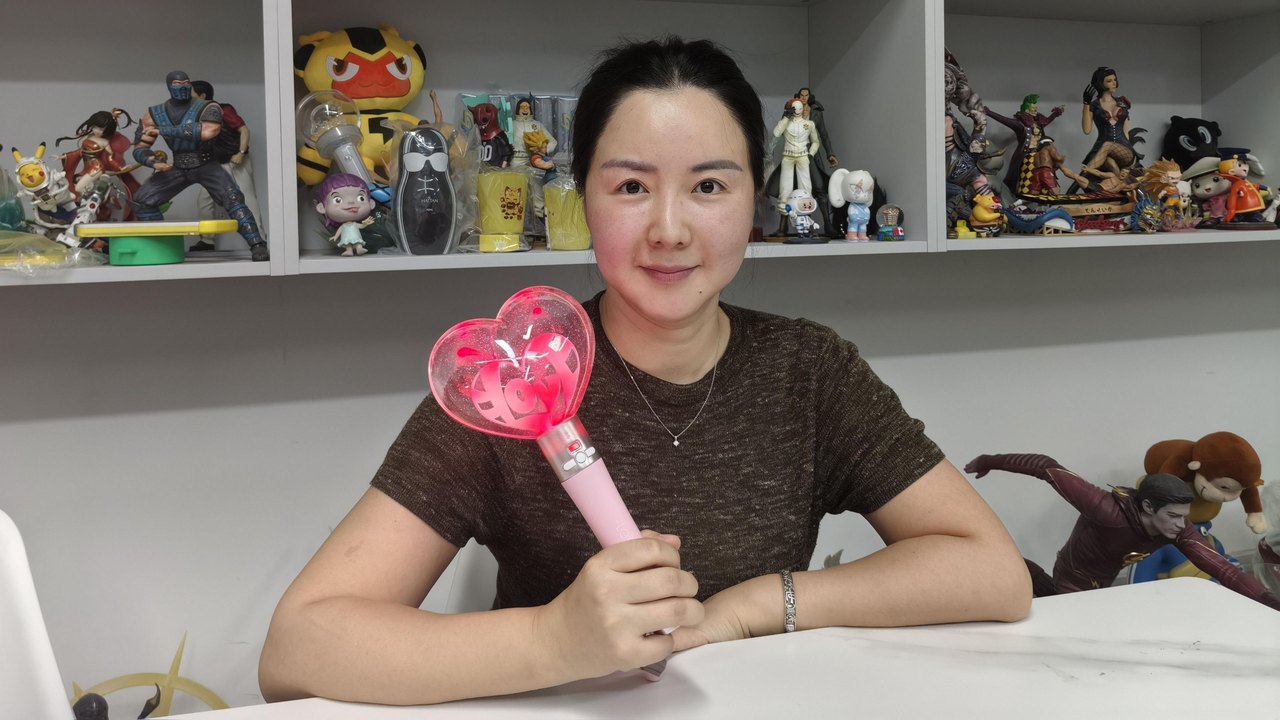 Melanie Wang from the Mihox sales team holds up a toy. She is sitting in front of shelves of other toys