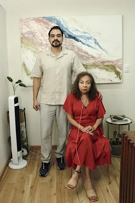 a mother with oxygen tubes in a red dress and son in a tan outfit stand for a portrait