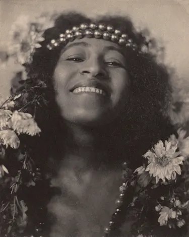 Lizzie Avery smiles, wearing a beaded headband and surrounded by flowers