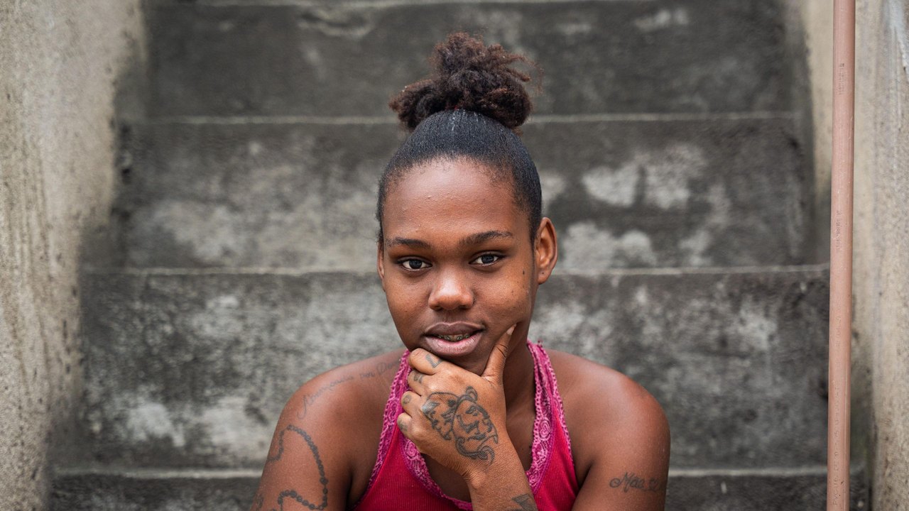 A young woman with a pink top sitting on concrete steps looking into the camera
