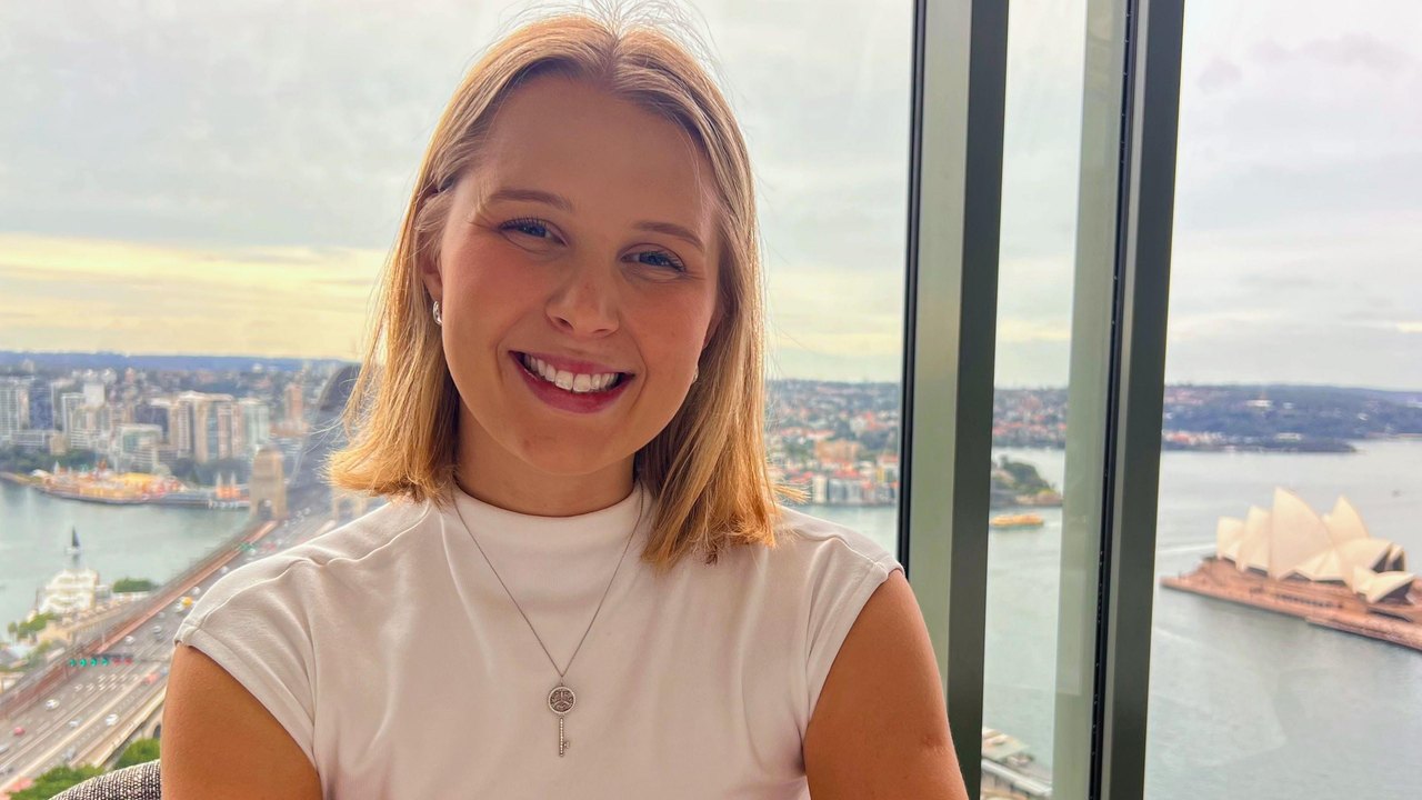 Rachel James stands in front of a window that looks over Sydney harbour and the Australian city's famous opera house
