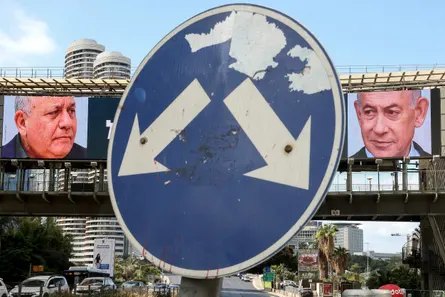 A weathered road sign stands before billboards showing Benjamin Netanyahu and Gadi Eisenkot