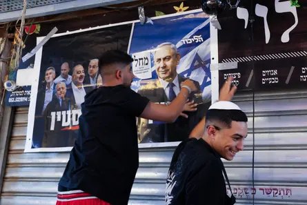 A supporter tapes up a poster of Netanyahu on a market shutter as another man smiles nearby