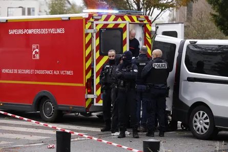 Police officers gather by a fire service vehicle and mortuary van in Trappes, France