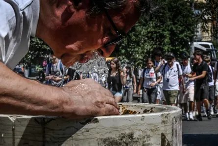 A man leans down to drink from a public fountain during hot weather in Naples