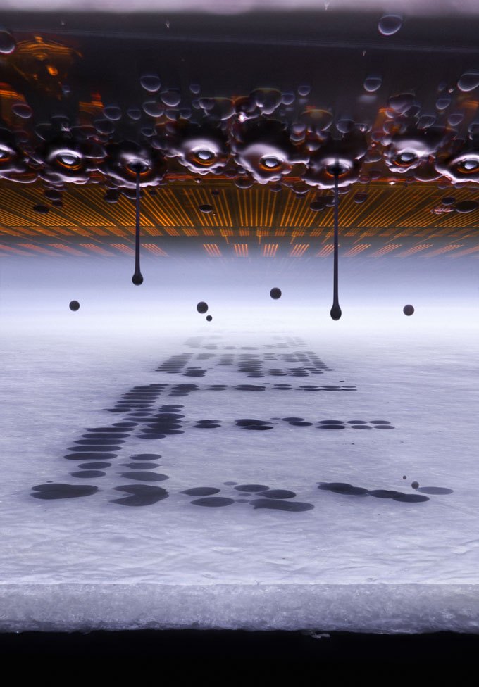Droplets of ink hang suspended between a printer’s nozzles and the paper below.