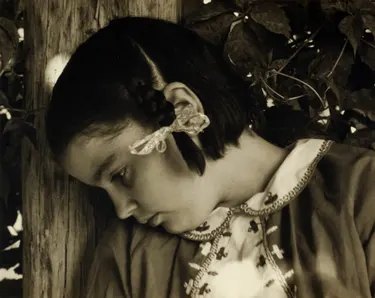 Miss Thomson rests her head against a wooden post, eyes downcast, amid leaves