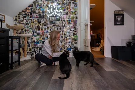 woman sits on floor next to two cats