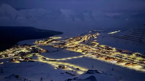 An illuminated village spread across a snowy valley at night, surrounded by dark mountains